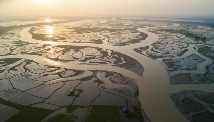 Воздушный снимок обширной дельты реки на рассвете. Вода подступает к сельскохозяйственным угодьям и постройкам.